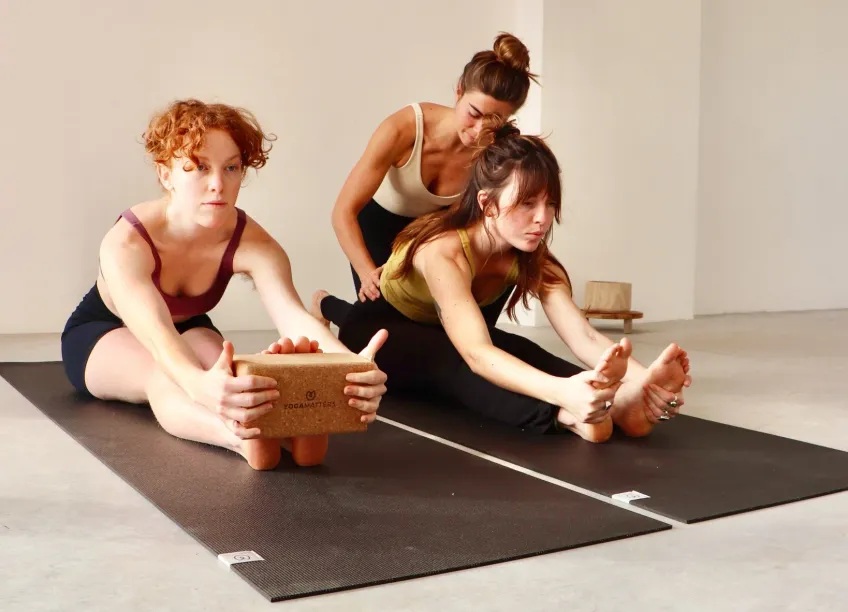 A teacher guiding two students through a seated forward fold